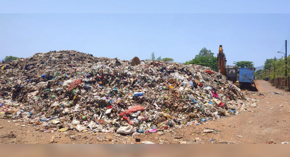Massive garbage pile at Ladvali dumping ground in Mahad, Raigad, with an excavator machine highlighting poor waste management conditions