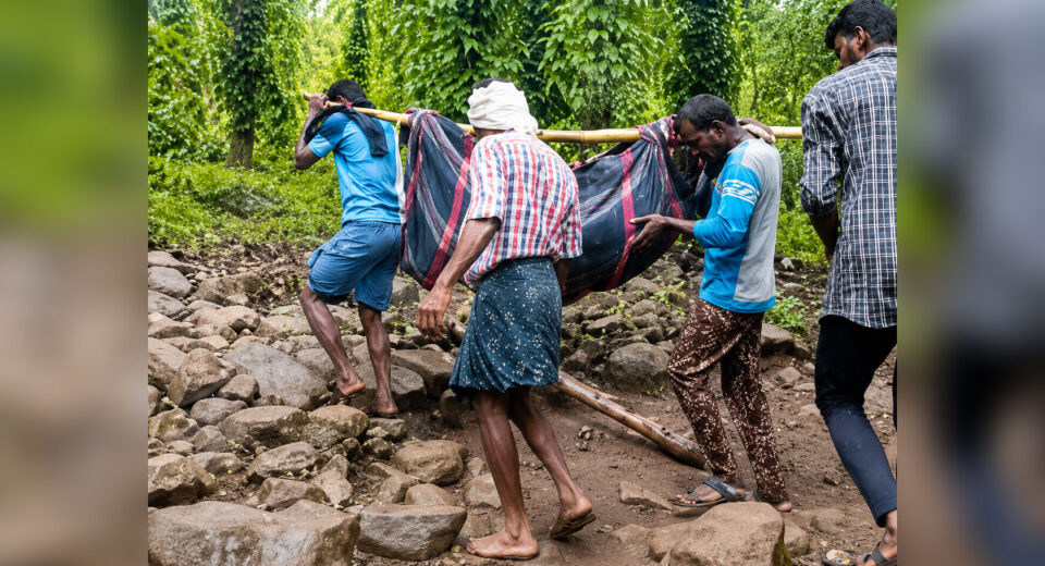 Villagers carrying a patient through difficult terrain in a remote tribal region of Maharashtra to access healthcare services.