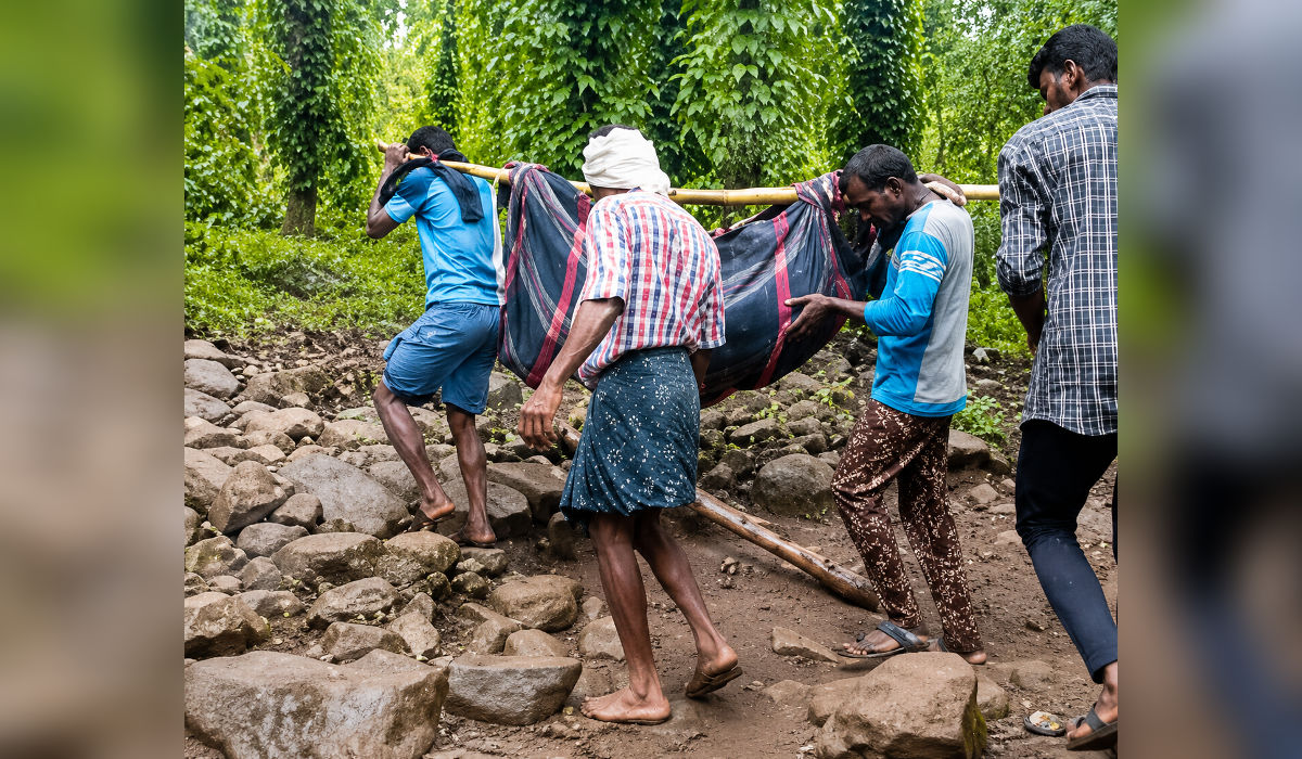 Villagers carrying a patient through difficult terrain in a remote tribal region of Maharashtra to access healthcare services.