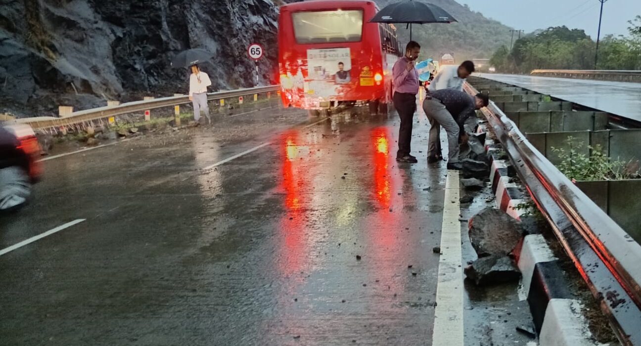 Large rocks and debris scattered on the Mumbai-Goa National Highway near Kemburli in Mahad after a landslide during heavy rain, with vehicles halted and commuters assessing the damage.