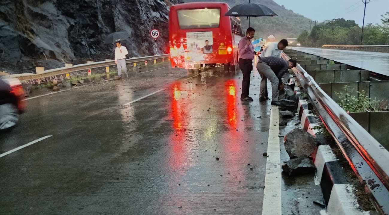 Large rocks and debris scattered on the Mumbai-Goa National Highway near Kemburli in Mahad after a landslide during heavy rain, with vehicles halted and commuters assessing the damage.